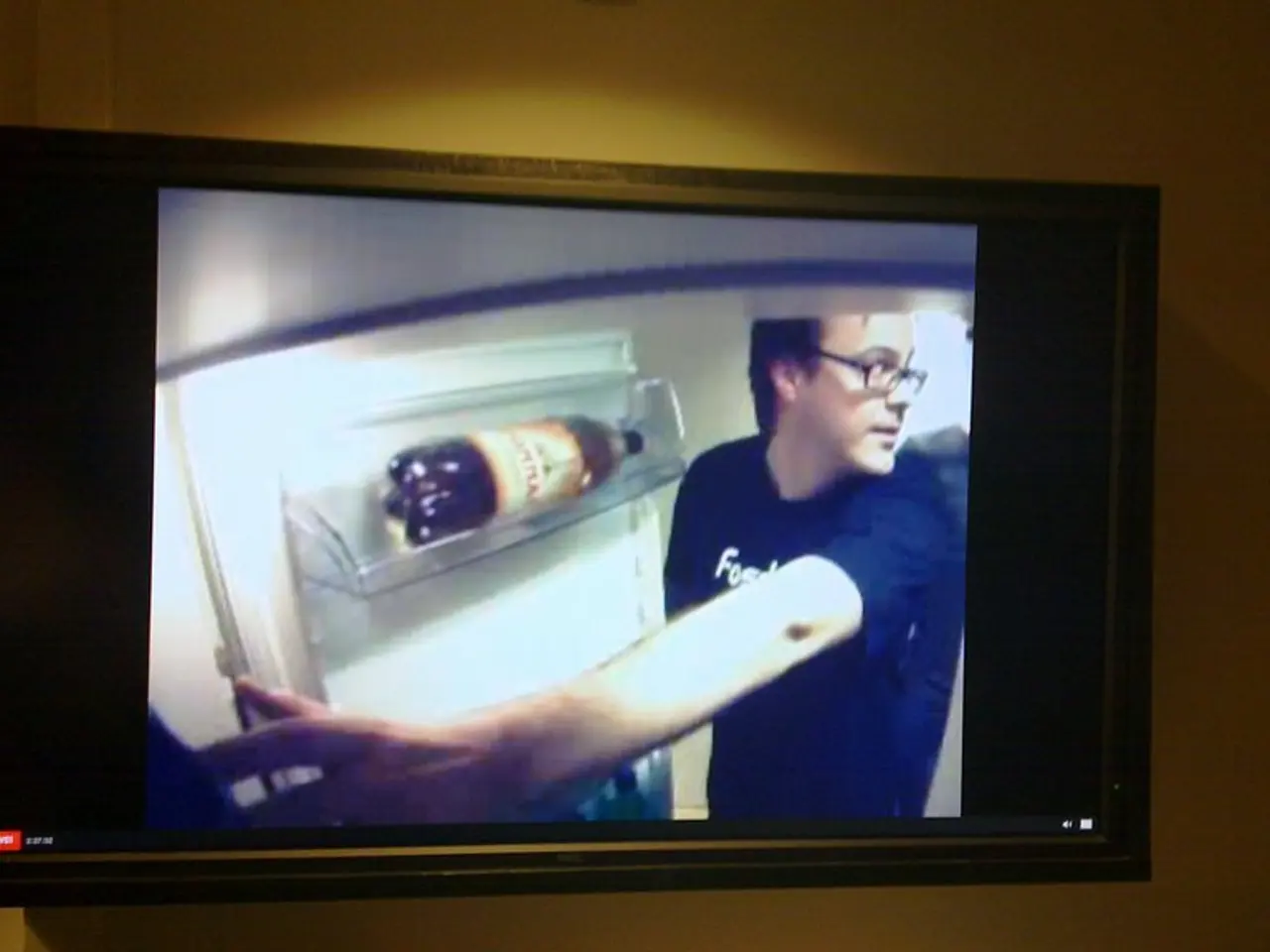 In this image there is a television attached to the wall, in which there is a person, refrigerator...