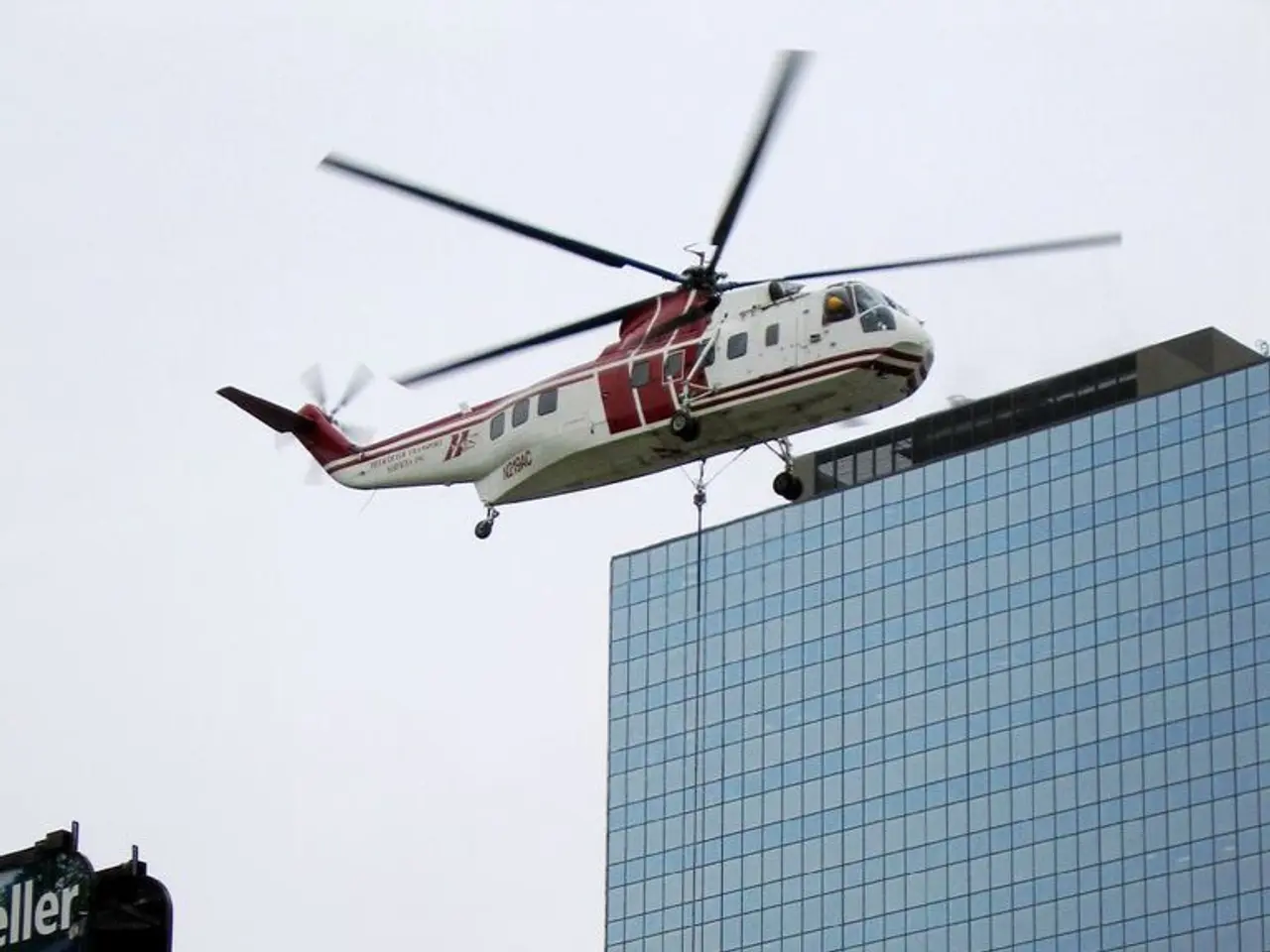 In this image there is a building, boards, pole, sky, helicopter and objects. Something is written...