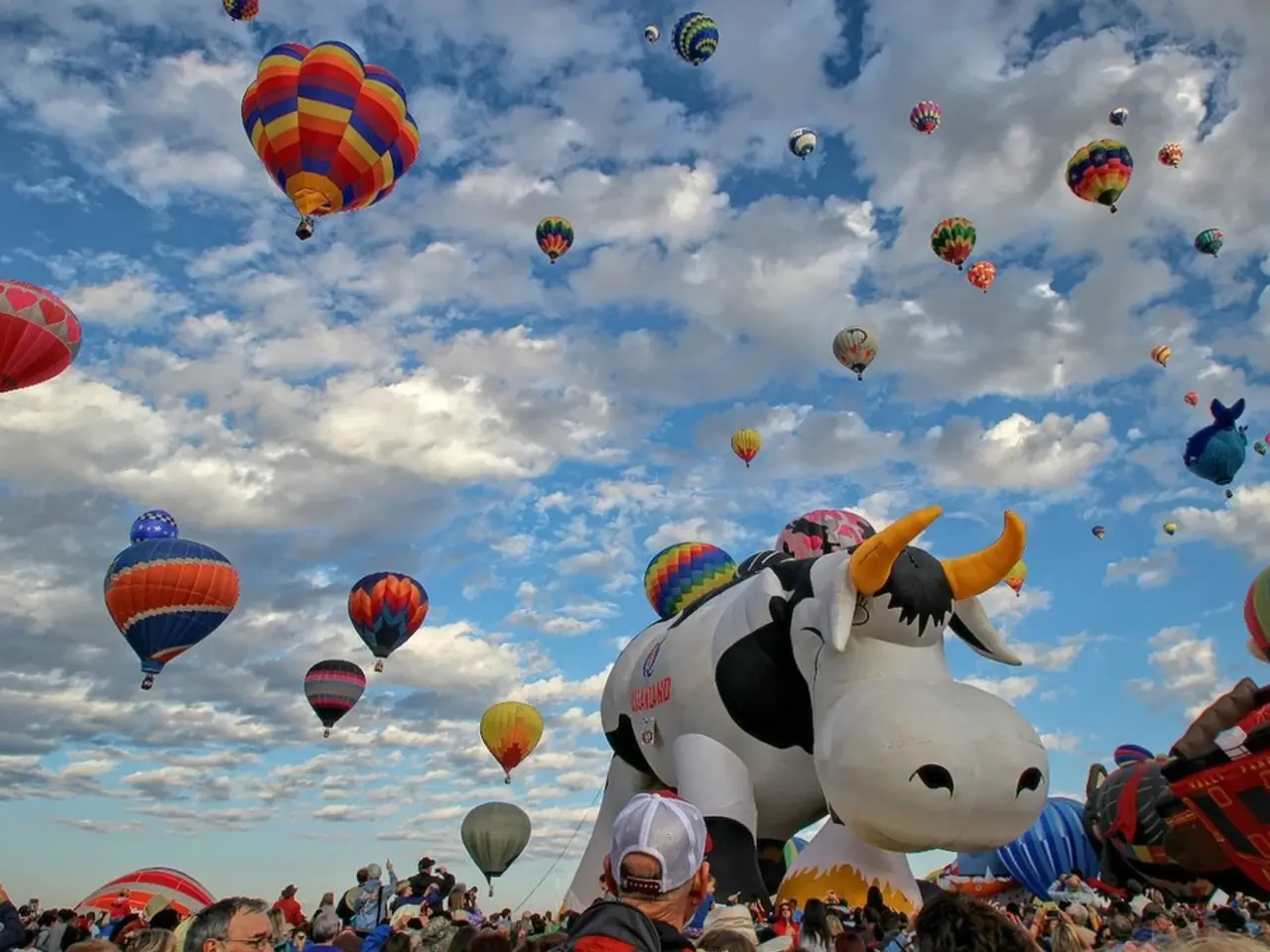 In this image we can see many air balloons in the air. In the background there is sky with clouds...