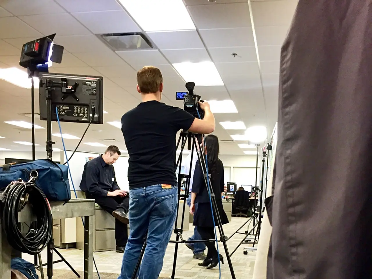 In the picture we can see an office floor, on it we can see a person holding a camera on the tripod...