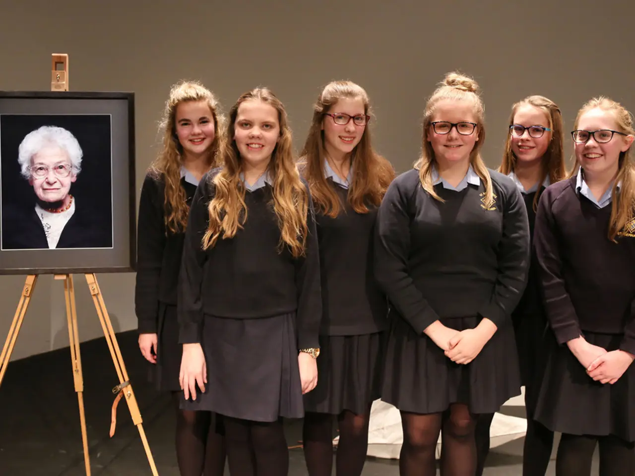 In this picture there are women standing and smiling, behind these women we can see white object on...