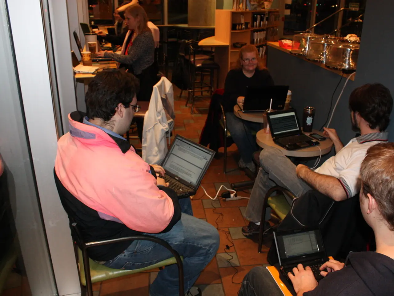 This image is clicked inside a room. There are tables and chairs. People are sitting on chairs. On...