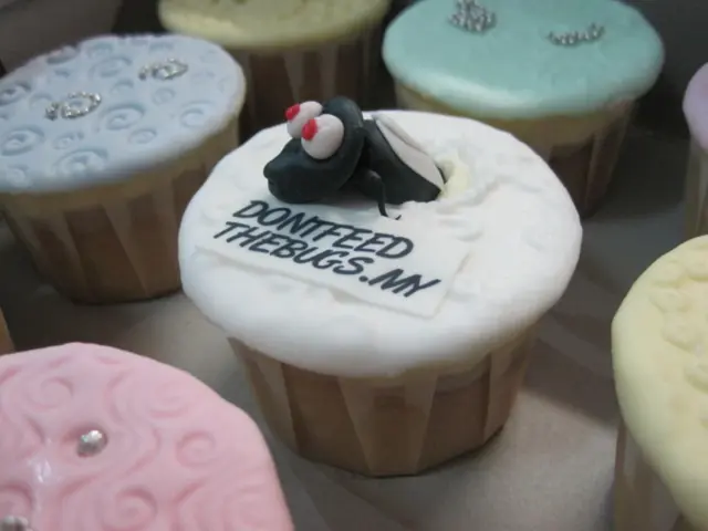 Here we can see cupcakes on a platform and on the middle cup cake there is a text and insect like...