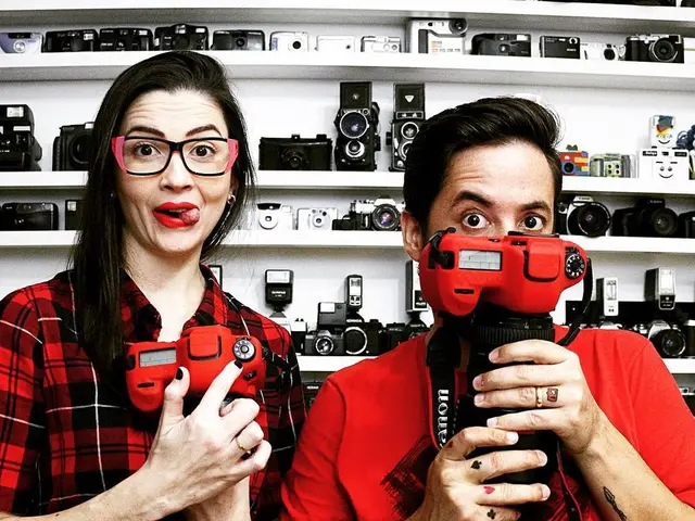 In this picture we can see a man and a woman holding cameras with their hands and in the background...