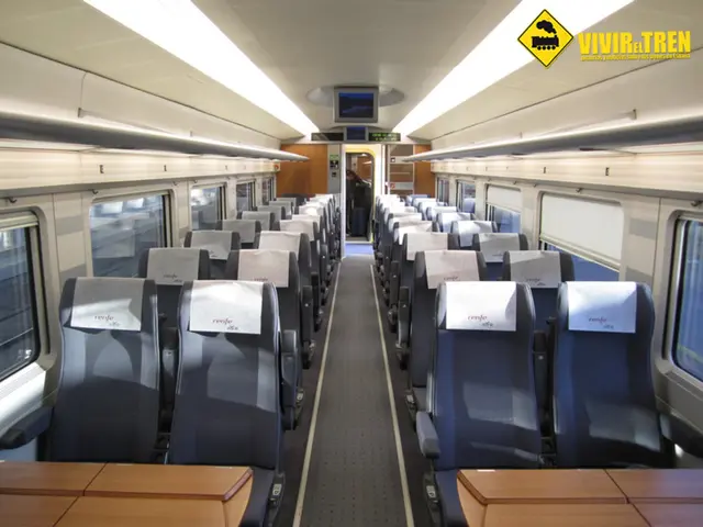 In this image we can see an interior view of a vehicle with seats and tables, a screen on the top...