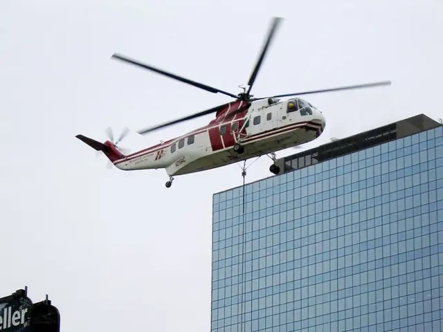 In this image there is a building, boards, pole, sky, helicopter and objects. Something is written...