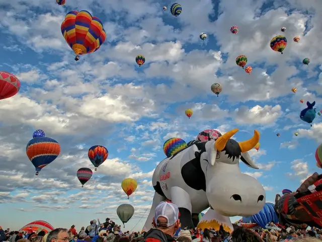 In this image we can see many air balloons in the air. In the background there is sky with clouds...