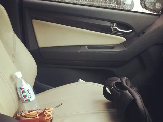 In the image the picture is taken inside a car, there is a car seat and on the seat there are some...