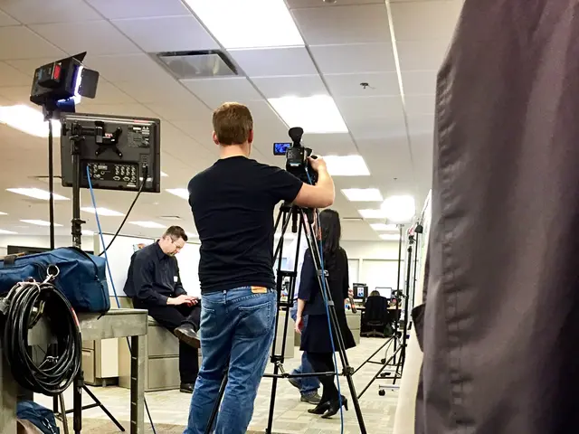 In the picture we can see an office floor, on it we can see a person holding a camera on the tripod...