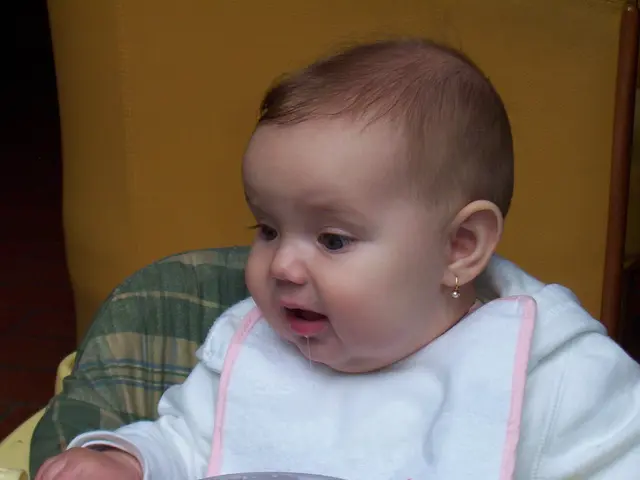 In this image we can see a child wearing white color dress is sitting on the baby chair.