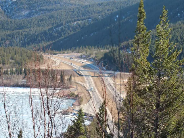 In this image we can see motor vehicles on the roads, river, hills and trees.
