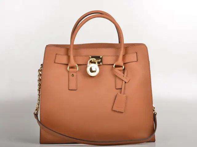 In this image there is a bag of brown colour having a lock in the middle and chain at the left...