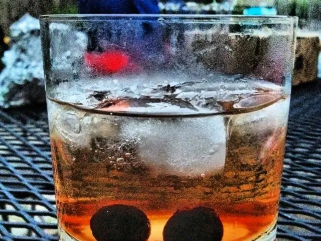 In this picture we can see a glass with drink and ice cubes in it and this glass is placed on a...