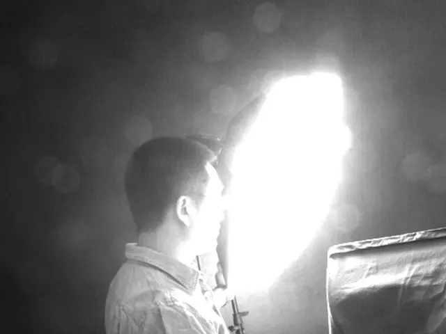 In this black and white picture we can see a person standing and holding 2 flashlight stands & an...